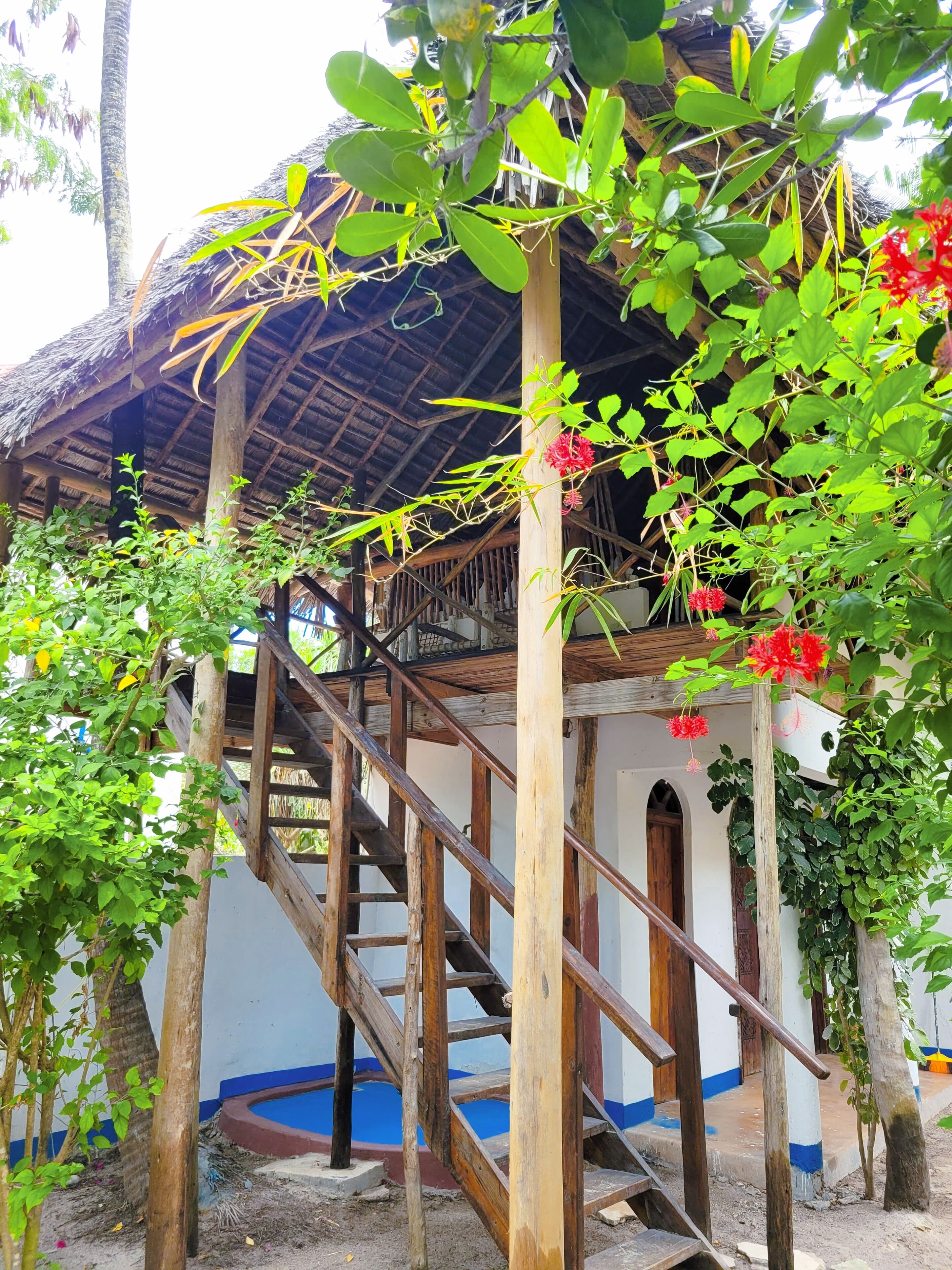 A wooden staircase leading to a thatched-roof structure with a blue-painted base.