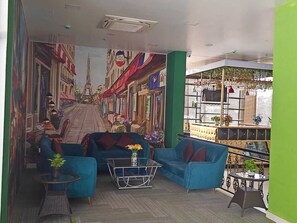 Habitación con un mural de una calle parisina, un sofá azul, una mesita de centro de cristal y un pequeño balcón con plantas.
