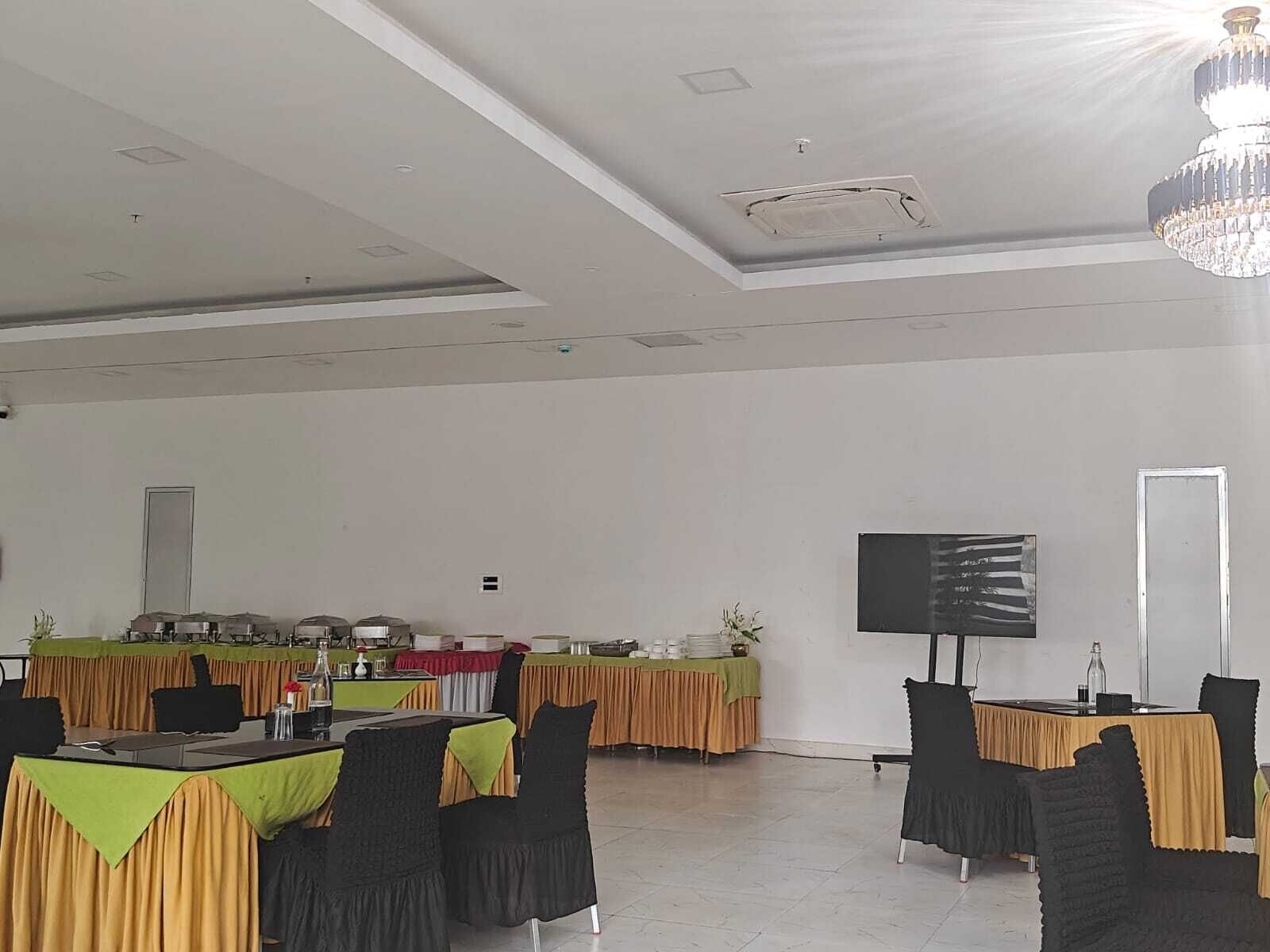 Un salón de conferencias con mesas, sillas, una lámpara de araña, un televisor de pantalla plana y una puerta.