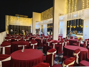 A banquet hall with round tables and chairs, decorated with drapes and lights. - Inventree Hotel The Monarch Bagalur  (Bengaluru)