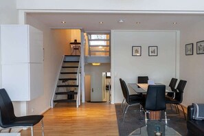 Ein modernes Interieur mit einer Treppe, einem Essbereich mit Tisch und Stühlen sowie einer Küchenzeile mit Kühlschrank.