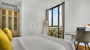 A hotel room with a bed, a desk, a chair, a large window, and a view of the city. - Karven by Kozystay - Cilandak (South Jakarta)