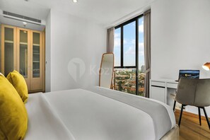 A hotel room with a bed, a desk, a chair, a large window, and a view of the city. - Karven by Kozystay - Cilandak (South Jakarta)