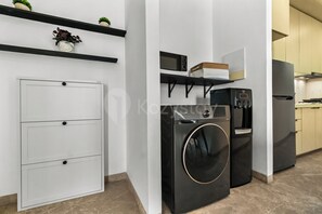 A compact kitchen with a built-in microwave, a black washing machine, and a refrigerator. - Karven by Kozystay - Cilandak (South Jakarta)