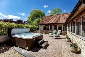 A hot tub in a backyard with a brick patio, a stone building, and a view of trees. - The Old Piggery at Rusty Lane Farm (Seend)