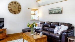 A living room with a leather sofa, wooden coffee table, and a large wall clock. - The Old Piggery at Rusty Lane Farm (Seend)