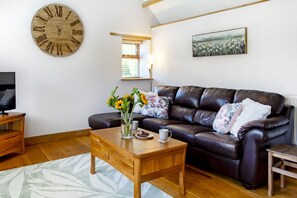A living room with a leather sofa, wooden coffee table, and a large wall clock. - The Old Piggery at Rusty Lane Farm (Seend)