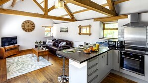 A modern kitchen with a central island, built-in appliances, and a dining area with a sofa and coffee table. - The Old Piggery at Rusty Lane Farm (Seend)