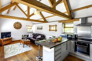 A modern kitchen with a central island, built-in appliances, and a dining area with a sofa and coffee table. - The Old Piggery at Rusty Lane Farm (Seend)