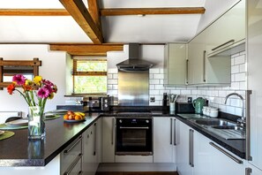 A modern kitchen with white cabinets, stainless steel appliances, and a wooden ceiling. - The Old Piggery at Rusty Lane Farm (Seend)