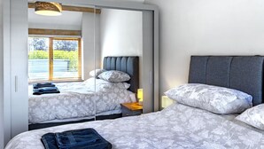 A bedroom with two beds, a wardrobe, and a window with blinds. - The Old Piggery at Rusty Lane Farm (Seend)