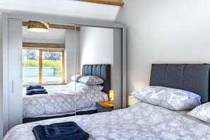 A bedroom with two beds, a wardrobe, and a window with blinds. - The Old Piggery at Rusty Lane Farm (Seend)