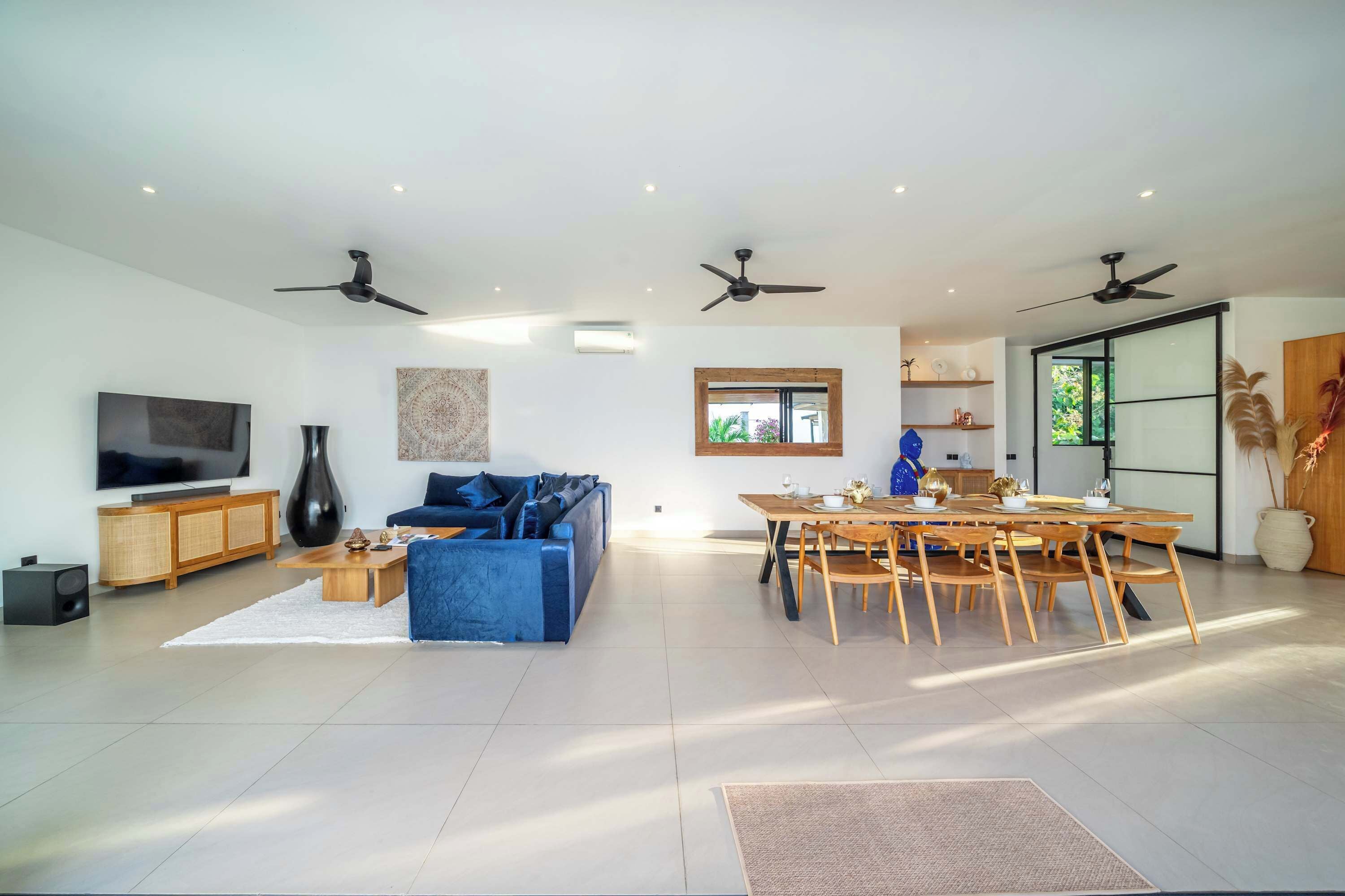 A spacious living area with a blue sofa, a dining table, and a TV.