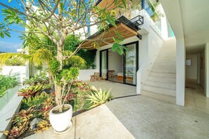 Ein modernes Haus mit Glastür, die auf einen Balkon führt, umgeben von üppiger tropischer Vegetation.
