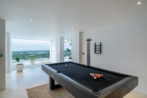 Ett modernt biljardbord för inomhusbruk med fri sikt ut mot omgivningen, en krukväxt och en minimalistisk väggdekoration.