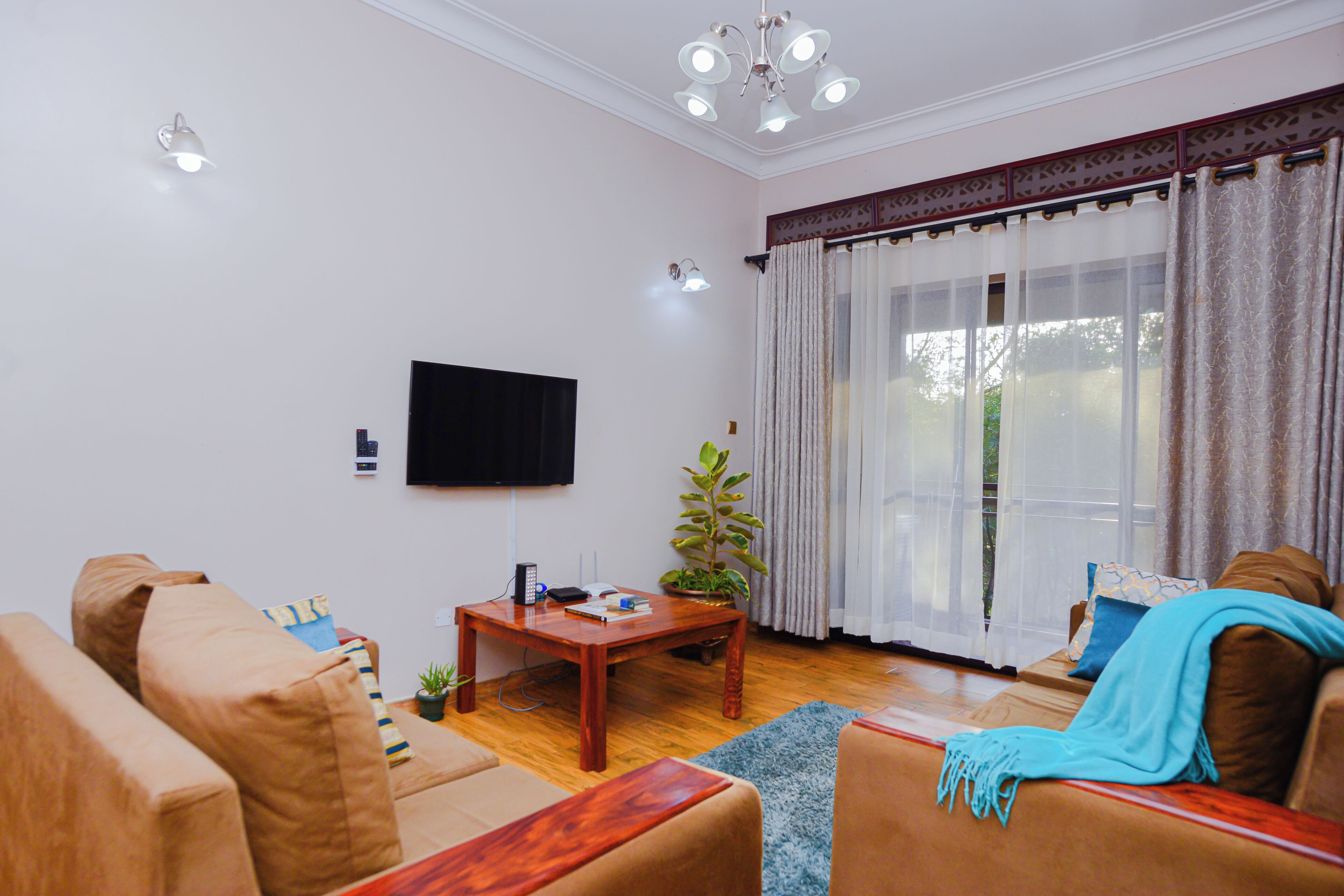 A living room with a flat-screen TV, a wooden coffee table, a sofa, and a large window with curtains.