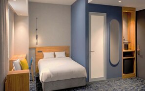 A hotel room with a bed, bedside table, lamp, wardrobe, and a door with a mirror.
