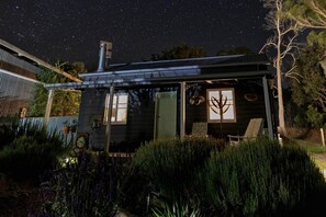 A small cabin with a covered porch, surrounded by dense shrubbery.