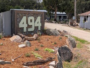 A sign with the number 494, surrounded by rocks and mulch, with a gravel path and buildings in the background.