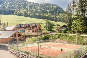 Eine Holzhütte mit Tennisplatz, umgeben von einer gebirgigen Landschaft.