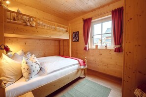 A wooden cabin bedroom with a bunk bed, a single bed, a window with curtains, and a green rug. - Chalet at the Zlaim lift with sauna (Grundlsee)