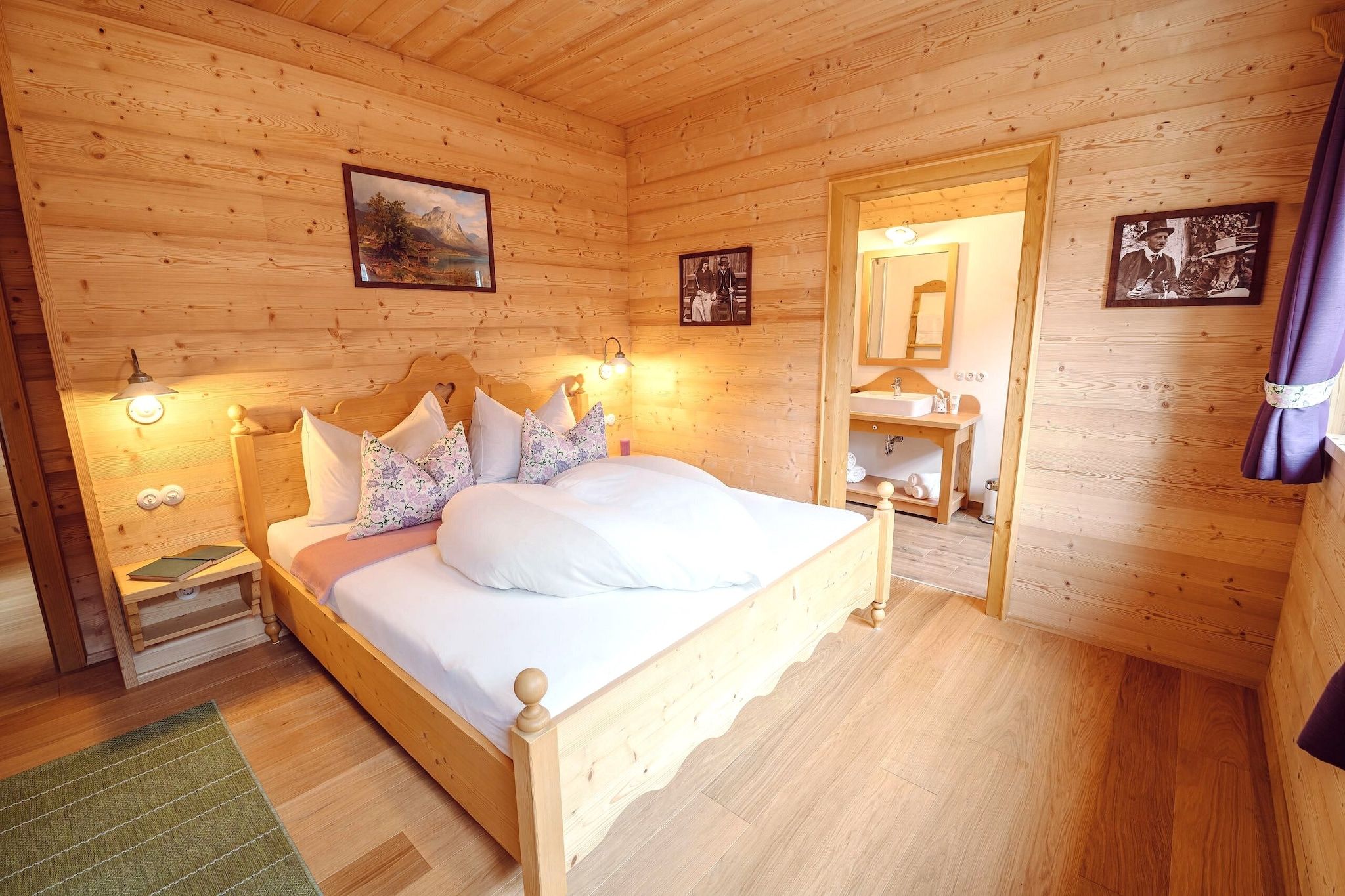 Une chambre à coucher dans un chalet en bois, avec un lit, des tables de chevet, des lampes fixées au mur et des tableaux encadrés.