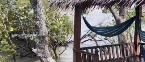 Una estructura de madera con techo de paja, una hamaca y una terraza de madera sobre el agua.