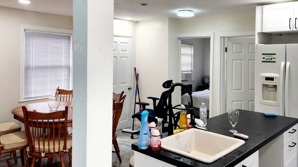 A kitchen with a black countertop, white cabinets, a water dispenser, and a dining area with a wooden table and chairs.
