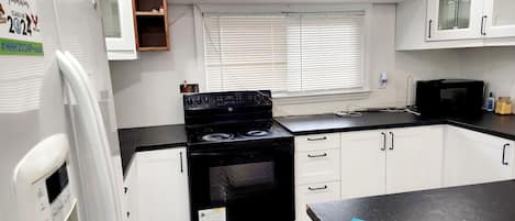 A compact kitchen with white cabinets, a black stove, and a microwave.