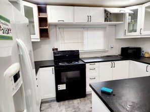 Una cocina compacta con gabinetes blancos, una estufa negra y un microondas.