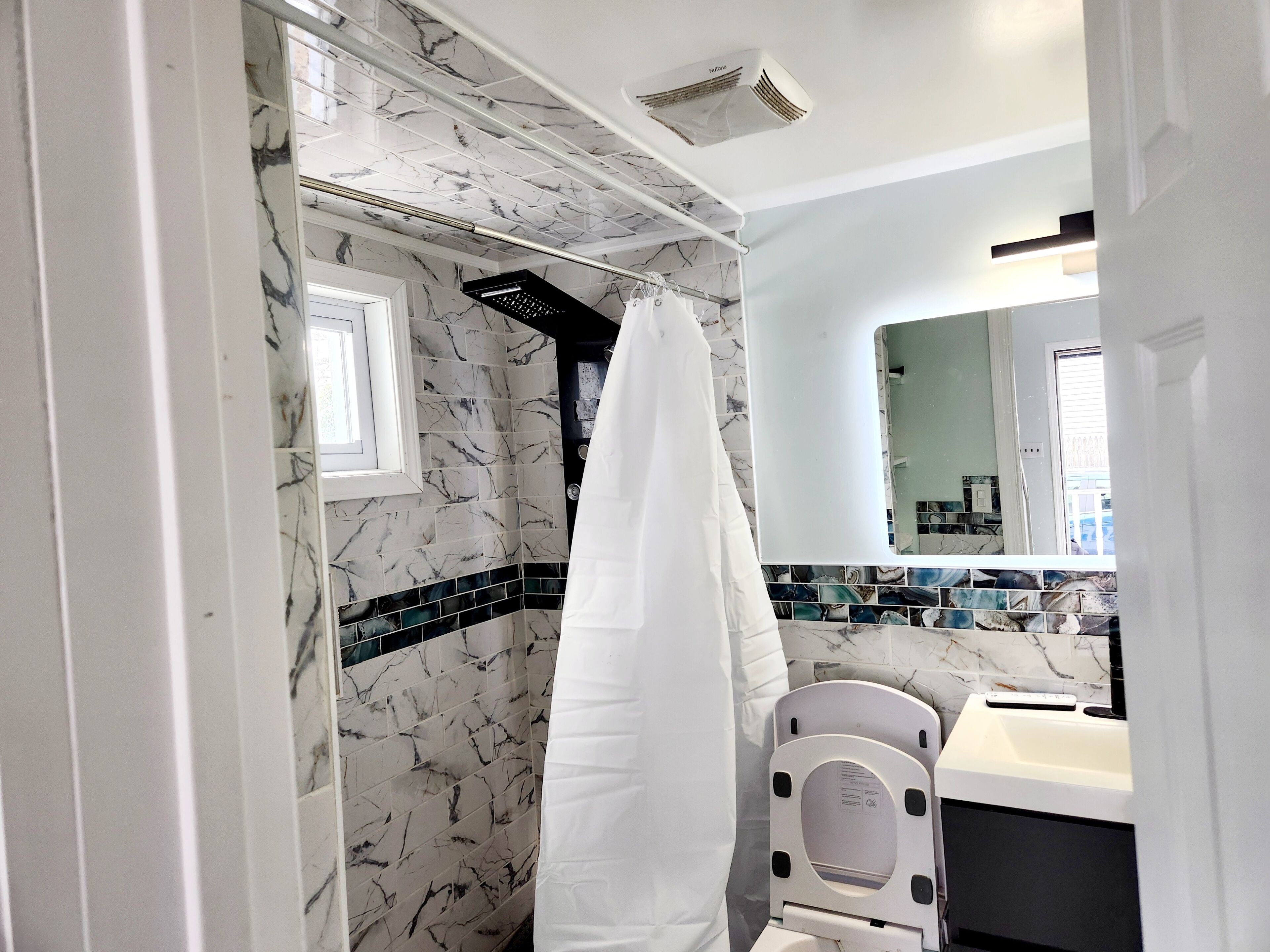 Een badkamer met een douche, wastafel, spiegel en handdoekhouder.