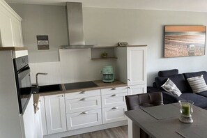Cocina compacta con muebles blancos, extractor de acero inoxidable y cafetera sobre la encimera.