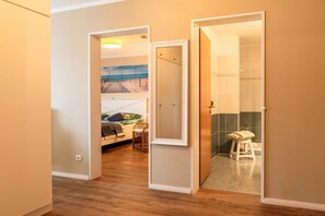 A room with a bed, a painting, a stool, and a door leading to a bathroom. - Bel blue, Residence Bel Vital (Binz)