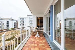 A balcony with a tiled floor, two wicker chairs, a small table with a vase, and a glass door leading to an indoor area. - Bel blue, Residence Bel Vital (Binz)