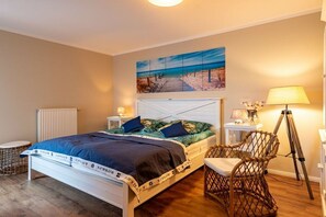 Ein Schlafzimmer mit einem Bett, einem Sessel, einer Lampe und einem Bild an der Wand.