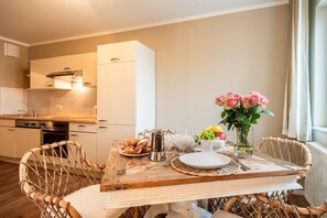A dining area with a wooden table set for breakfast, surrounded by wicker chairs. - Bel blue, Residence Bel Vital (Binz)