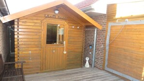 En stuga byggd av trä, med en trädörr, en bänk och en liten veranda.