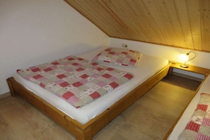 Una cama individual con colcha, una lámpara de noche y un cabecero de madera en una habitación con techo inclinado.