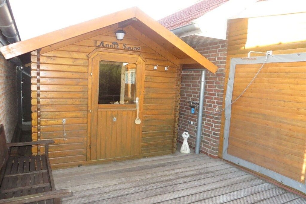 Eine Holzhütte mit Holztür, einer Bank und einem kleinen Veranda-Bereich.