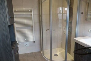 A bathroom with a glass-enclosed shower, a white sink, and a towel rack. - Annis Huus right on the water (Timmel)