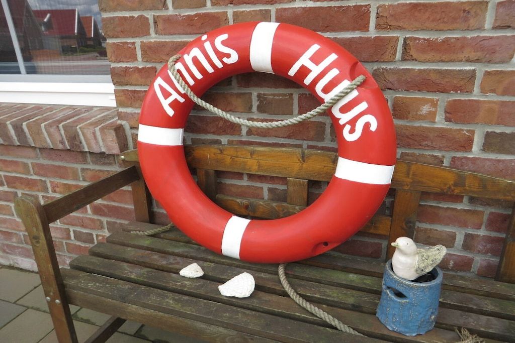 En livboj med inskriptionen ”Huis” placerad mot en tegelvägg, och som ligger på en träbänk tillsammans med en fågelskulptur.