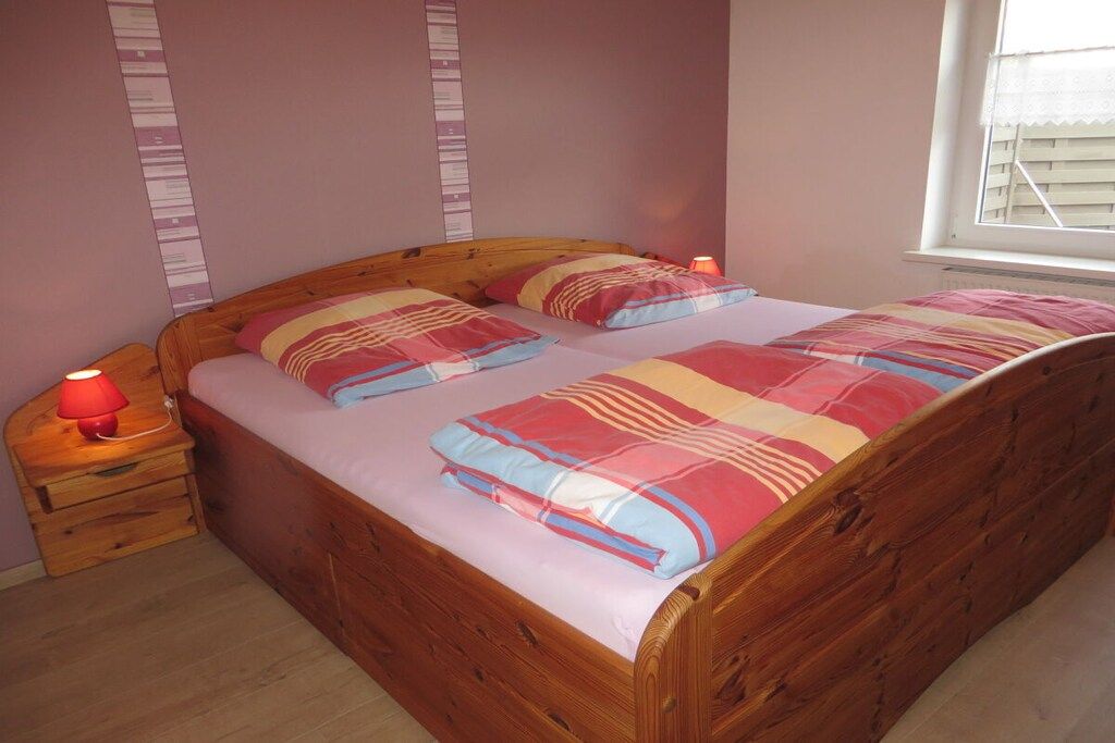 A single bed with a wooden frame and a colorful bedspread. There is a nightstand with a red lamp beside the bed.