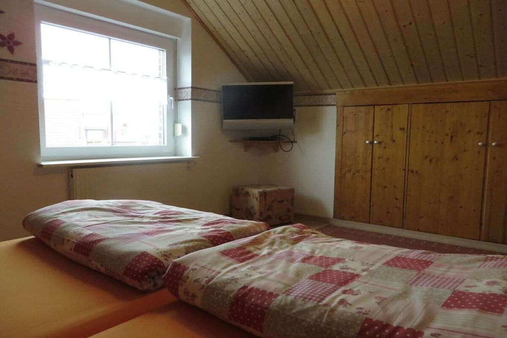 Una camera da letto con due letti, una finestra, soffitto in legno e TV a parete.