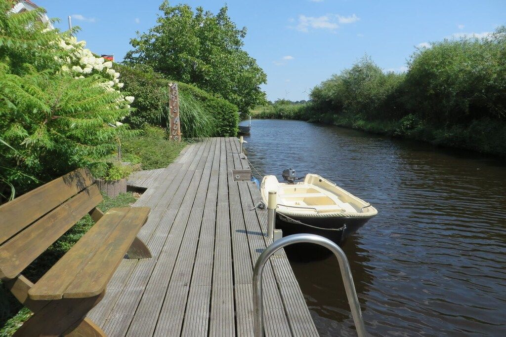 A wooden dock with a boat moored at the end, surrounded by greenery and a calm river.
