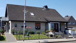 A two-story house with a tiled roof, a front door, and a small front yard with a fence and potted plants. - Apartment in Kappeln with swimming pool (Kappeln)
