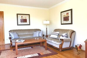 Ein Wohnzimmer mit einer Couch, einem Sessel, einem Couchtisch und zwei gerahmten Bildern an der Wand.