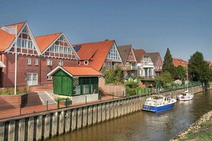 A canal-side building with a red-tiled roof, a green door, and a boat docked nearby. - "Apple Orchard" G. Armhold (Mittelnkirchen)