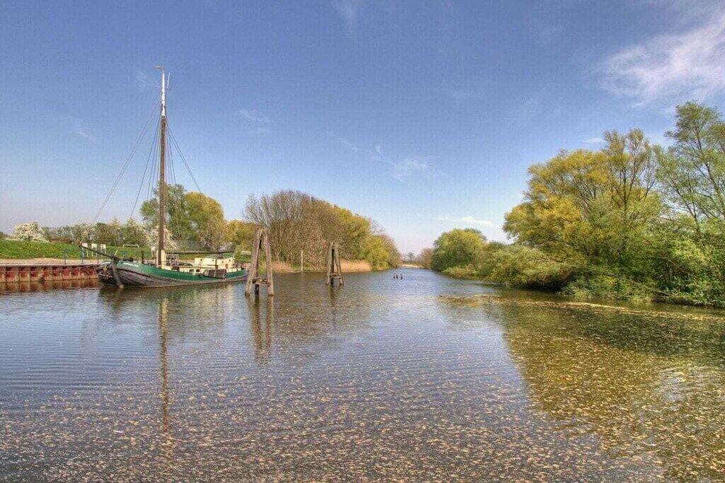 Une rivière paisible, avec un bateau amarré sur la rive gauche, entourée d’arbres et de verdure.