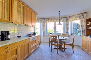 A kitchen with wooden cabinets, a tiled backsplash, a dining table with chairs, and a window with curtains.