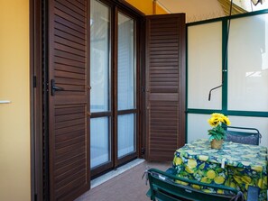 A room with a sliding glass door, a small table with a floral tablecloth, and a chair. - The Window Overlooking the Sea (Luni Mare)